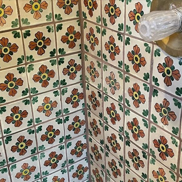 The corner of a tiled wall featuring a vibrant, retro floral pattern in orange, green, and yellow on each tile, creating a lively and detailed surface.