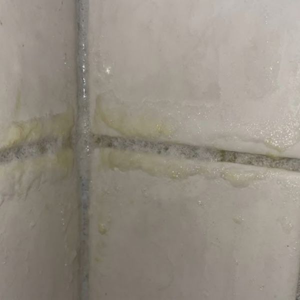 buildup of white hazy soap scum on grout lines in a tiled shower corner