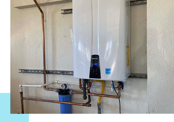 A professional installation of a white Navien tankless water heater on a wall, showing complex copper piping and a blue water filtration housing below.