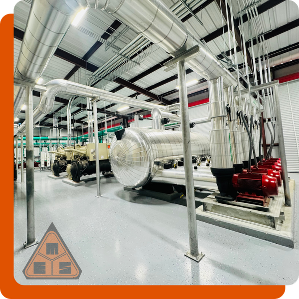 Clean industrial mechanical room with large, insulated pipes for a chiller system, showcasing complex conduit work and red pump motors.