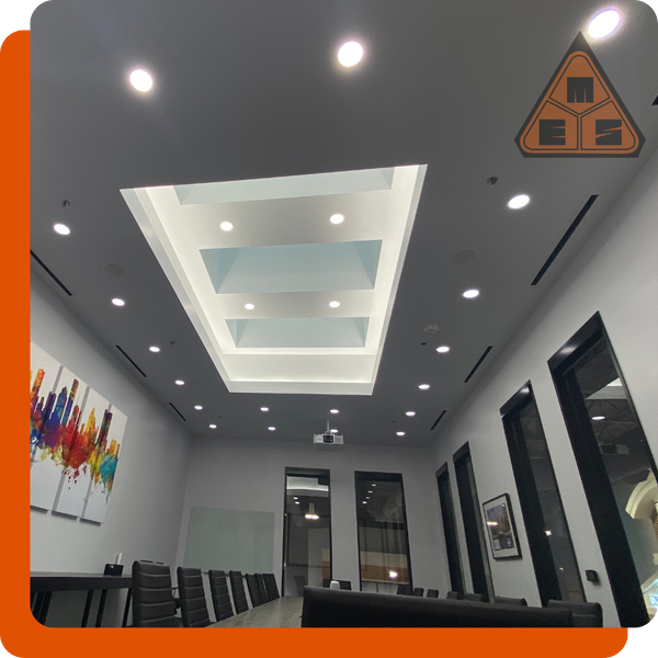 Modern commercial conference room with sophisticated architectural lighting, including a custom coffered ceiling fixture and recessed spotlights.