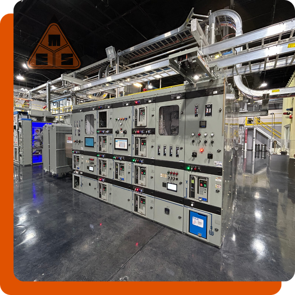 Large industrial electrical switchgear and motor control center (MCC) in a warehouse facility with a conveyor system in the background.