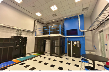 A modern data center with server racks and UPS systems, featuring complex overhead electrical conduit and cable trays.