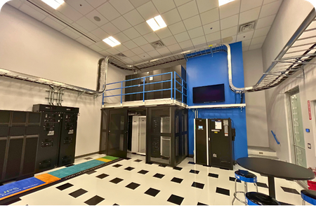 A modern data center with server racks and UPS systems, featuring complex overhead electrical conduit and cable trays. A modern data center with server racks and UPS systems, featuring complex overhead electrical conduit and cable trays.