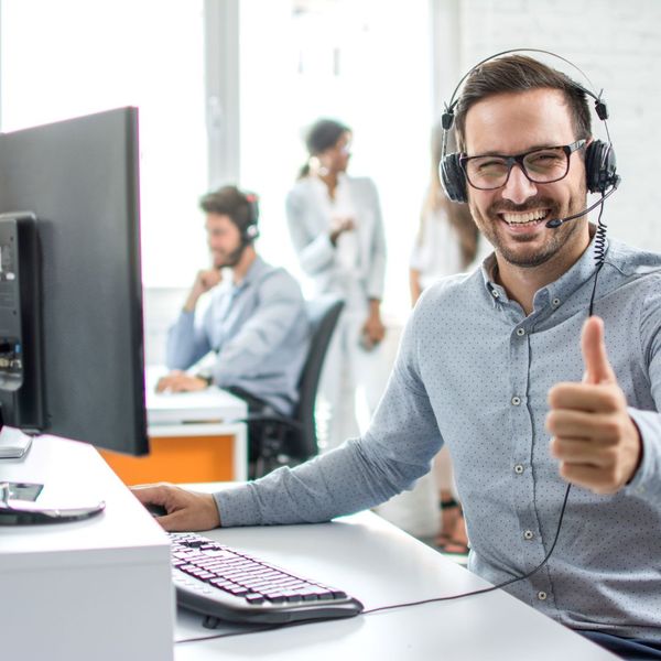 a person in front of a computer on a headset giving a thumbs up