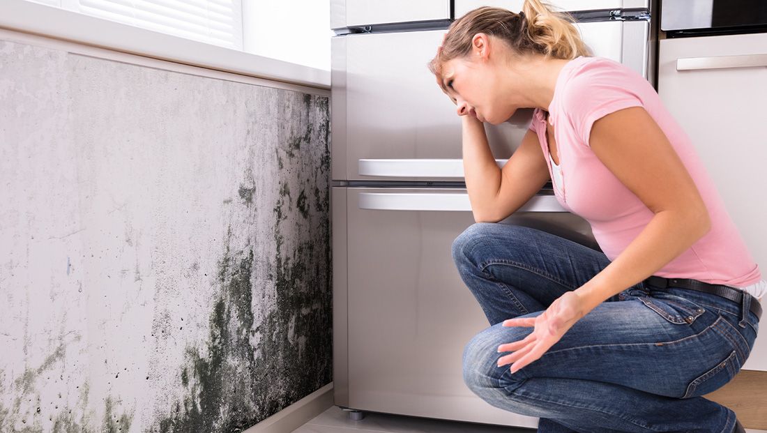 a person holding their head looking at a wall of mold