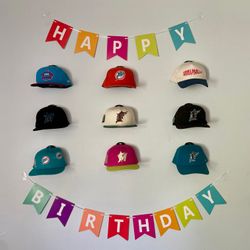 A real fan baseball cap collection displayed front-facing on a wall using The Original Squatchee™ adhesive hat hooks. Fan Hat Wall Display
