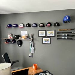 A real fan baseball cap collection displayed front-facing on a wall using The Original Squatchee™ adhesive hat hooks. Fan Hat Wall Display