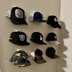 A real fan baseball cap collection displayed front-facing on a wall using The Original Squatchee™ adhesive hat hooks. Fan Hat Wall Display