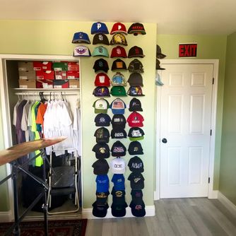 A real customer baseball cap collection displayed using The Original Squatchee™ adhesive hat hooks. Customer Hat Wall Display