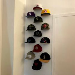 A real fan baseball cap collection displayed front-facing on a wall using The Original Squatchee™ adhesive hat hooks. Fan Hat Wall Display