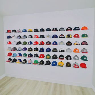 A full wall of baseball caps displayed front-facing as part of a finished bedroom, office, or entertainment space using The Original Squatchee™ patented adhesive hat hooks. Baseball Cap Wall Room Display