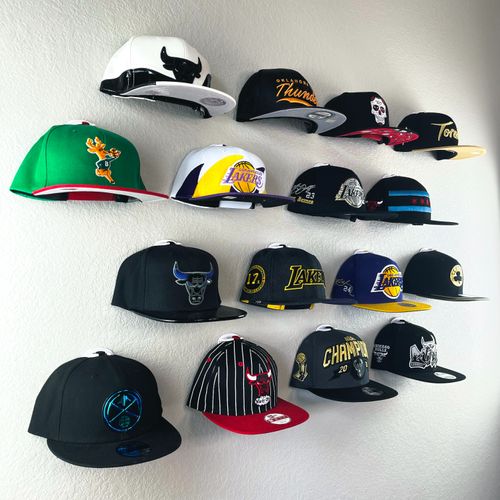 An NBA baseball cap collection displayed in a clean, front-facing arrangement using The Original Squatchee™ adhesive hat hooks. NBA Hat Wall Display Using The Original Squatchee™