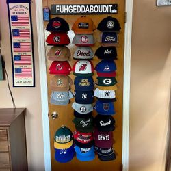 A real fan baseball cap collection displayed front-facing on a wall using The Original Squatchee™ adhesive hat hooks. Fan Hat Wall Display