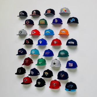 A collection of sports baseball caps displayed front-facing in a man cave, basement, or game room using The Original Squatchee™ adhesive hat hooks. Sports Baseball Cap Wall Display