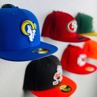 A small collection of NFL baseball caps displayed front-facing on a wall using The Original Squatchee™ patented adhesive hat hooks. Small Baseball Cap Wall Display