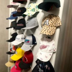 A real fan baseball cap collection displayed front-facing on a wall using The Original Squatchee™ adhesive hat hooks. Fan Hat Wall Display