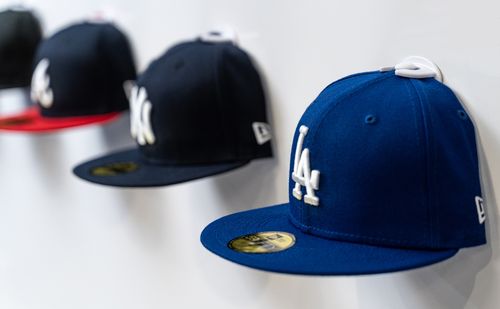 Blue and black baseball caps displayed front-facing on a white wall using white Squatchee™ adhesive hat hooks. Baseball caps displayed on a wall with Squatchee™ adhesive hat hooks