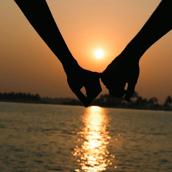 Close-up of two people holding hands while watching a sunset.