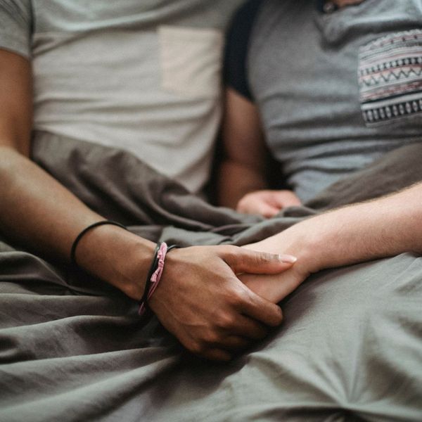 A couple sitting together in a bed, holding hands.