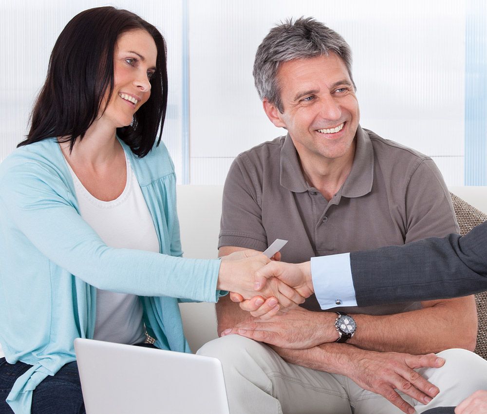 a happy couple shaking hands with someone in front of a laptop