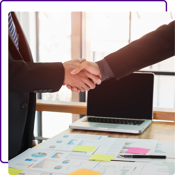 handshake, laptop and papers with graphs on desk