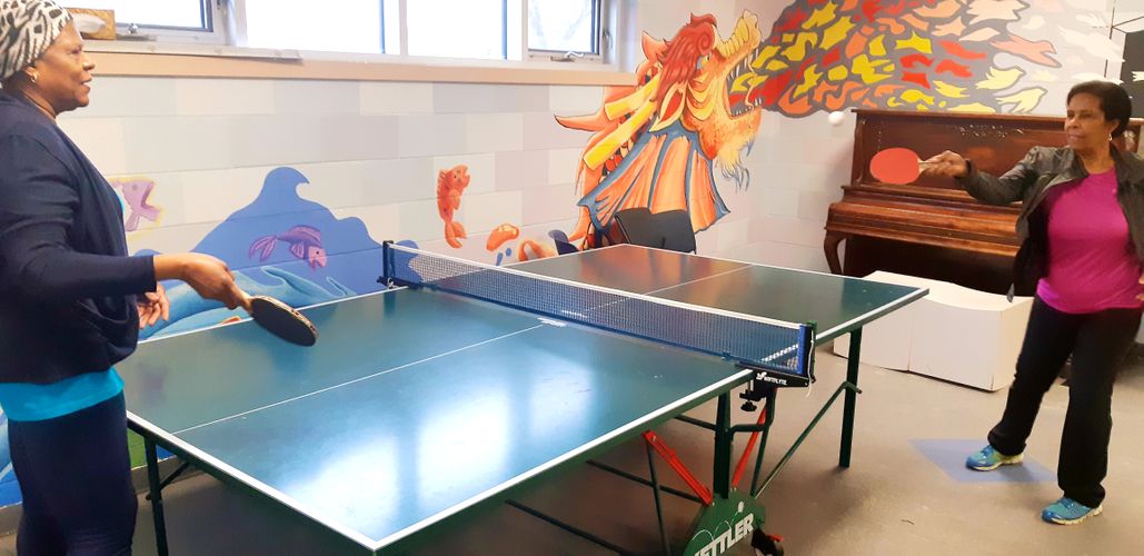 two senior ladies play ping pong inside recreation room