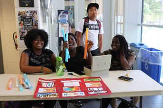 Youths are smiling and selling ice popsicles. The girl in the middle holds them up to offer you one.