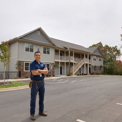 A smiling maintenance team member standing proudly near the apartment building.