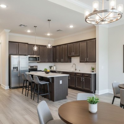 An empty, modern communal kitchen and dining area features dark cabinetry, a large island, and round tables with chairs.
