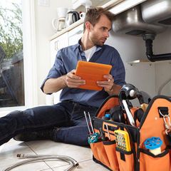 plumber inspecting a sink while holding a tablet