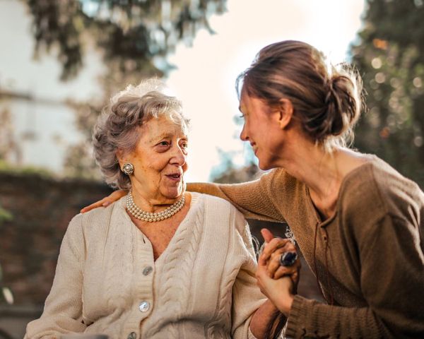 An elderly woman speaking with a young woman