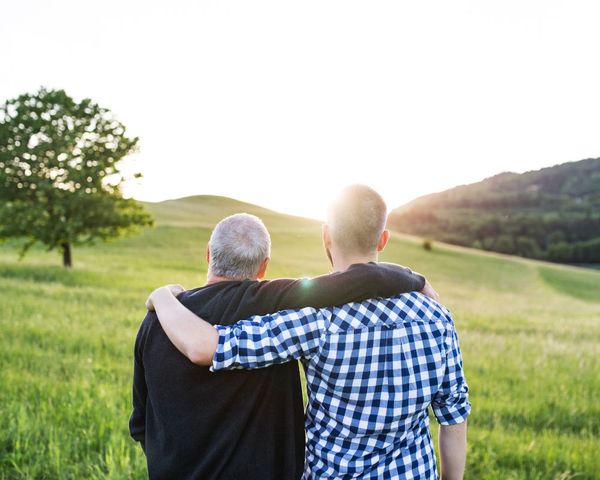 An elderly father and son with their arms around each other as they look at the landscape 