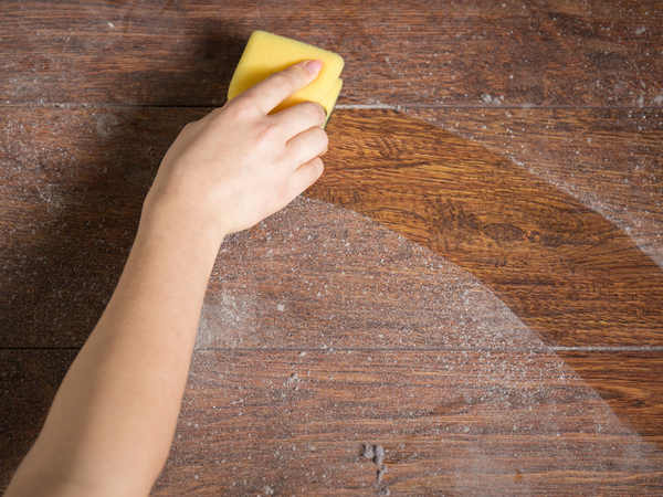 An arm using a sponge to wipe away dirt and dust from a wooden surface.