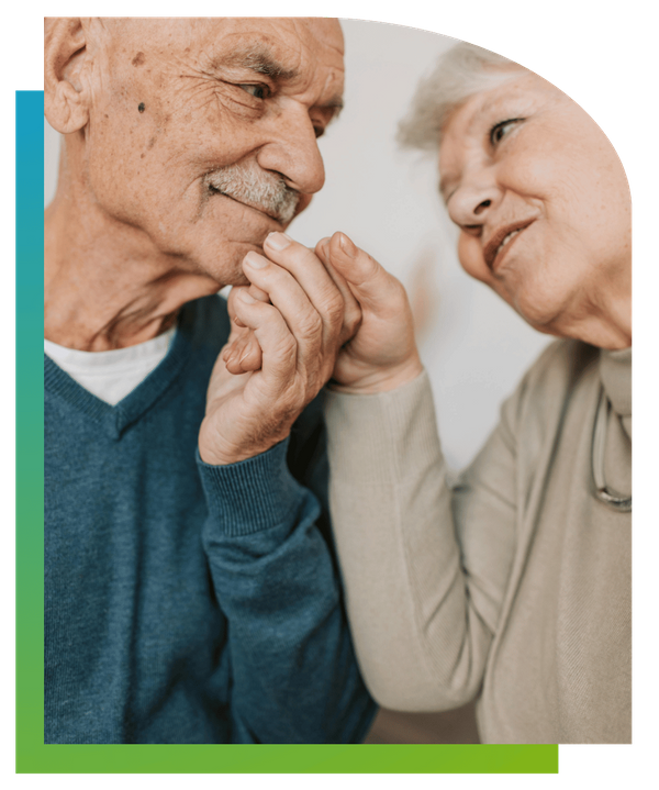An elderly couple holding hands and looking affectionately at each other.