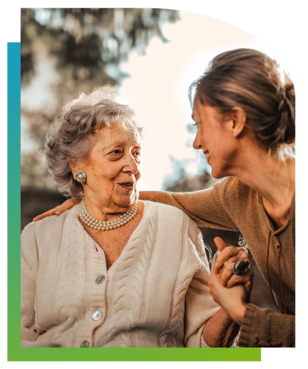 A younger woman placing her arm around an elderly woman's shoulder as they talk outdoors.