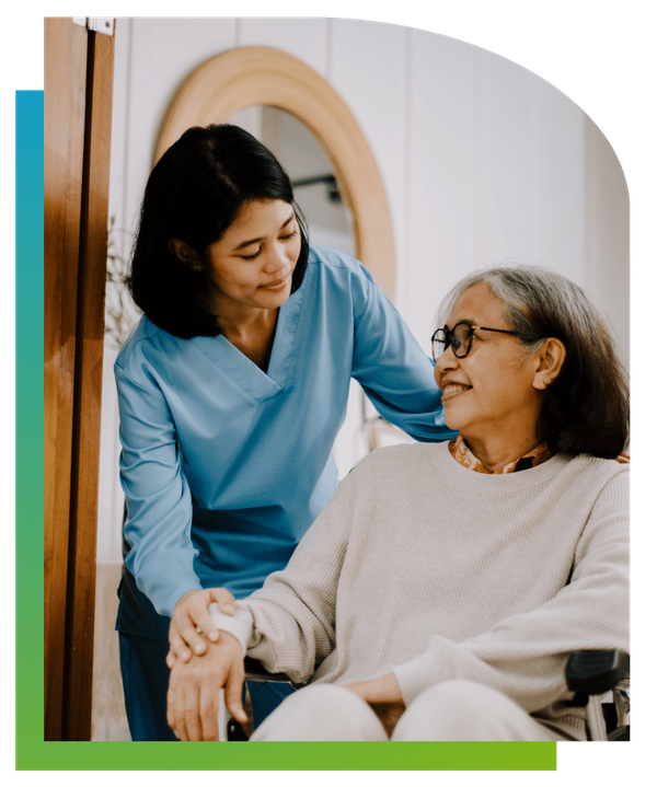 A female healthcare worker or caregiver smiling and supporting an elderly woman sitting down.