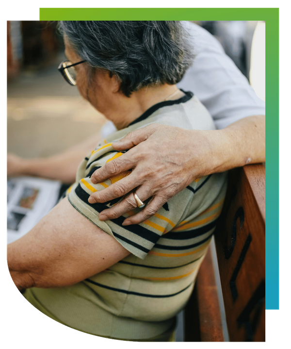 Close-up of a caregiver placing a comforting hand on an elderly person's shoulder.