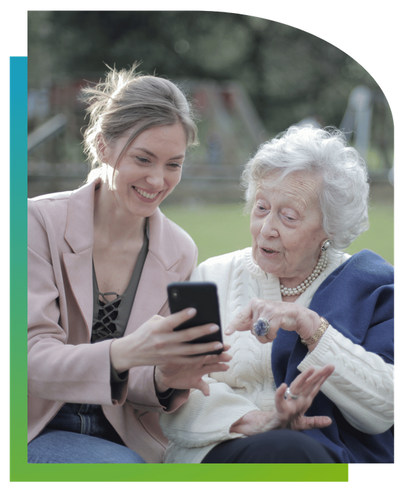 A young woman showing something on her smartphone to an elderly woman, both smiling.