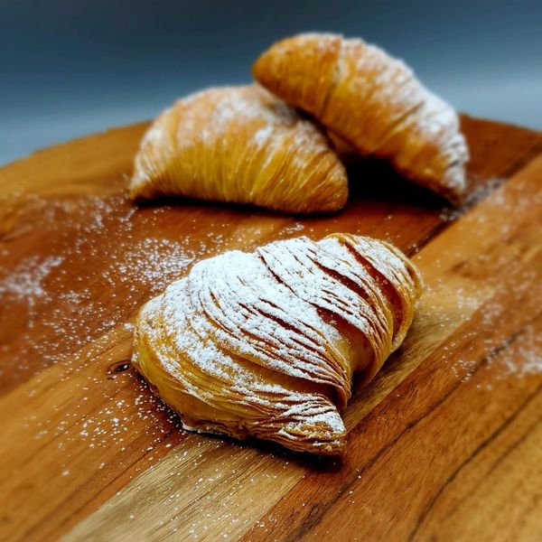 Three powdered sugar-dusted sfogliatelle pastries on a wooden cutting board. Three powdered sugar-dusted sfogliatelle pastries on a wooden cutting board.