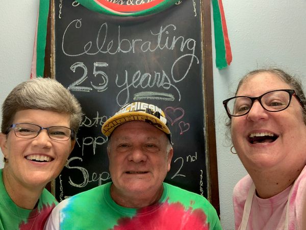 three happy employees in front of a 25 year anniversary sign