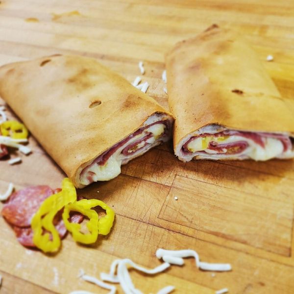 Two halves of a savory Italian calzone, revealing meat and cheese filling, on a wooden surface with scattered ingredients. Two halves of a savory Italian calzone, revealing meat and cheese filling, on a wooden surface with scattered ingredients.