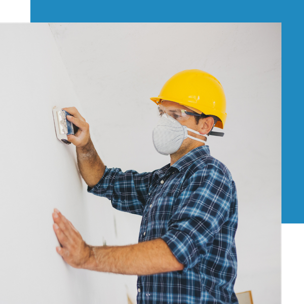 person sanding drywall with hardhat and mask