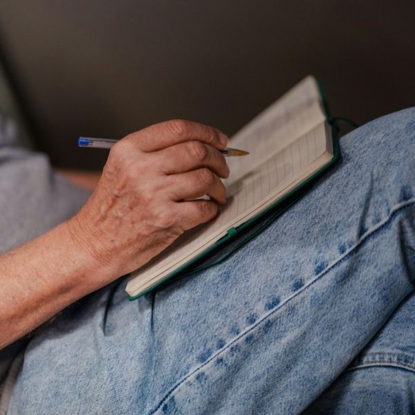 Person sitting and journaling with a blue pen.