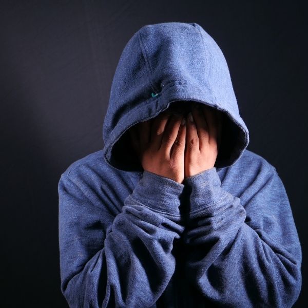 person with hood on with hands covering face