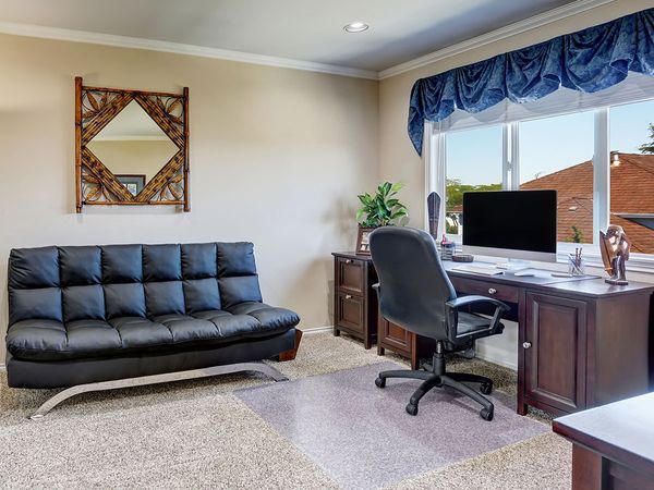 Luxury interior of home office with modern black leather sofa and bamboo frame mirror above.