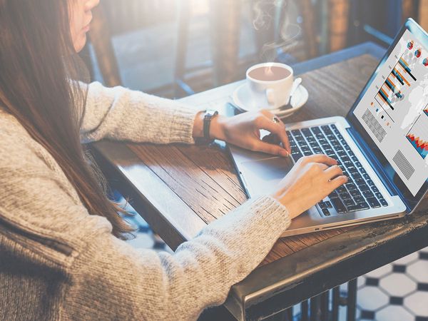 Woman looking at charts and graphs on a laptop inside a cafe.