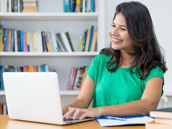 Young woman laughing while working at her computer desk at home.