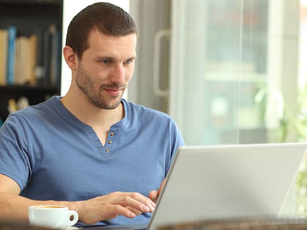 Serious adult man using a laptop browsing web sitting in a coffee shop.