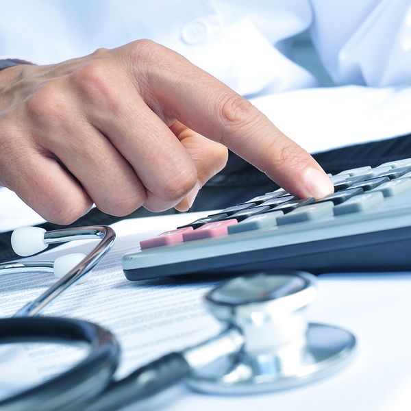 Closeup of a young caucasian healthcare professional wearing a white coat and using a calculator.